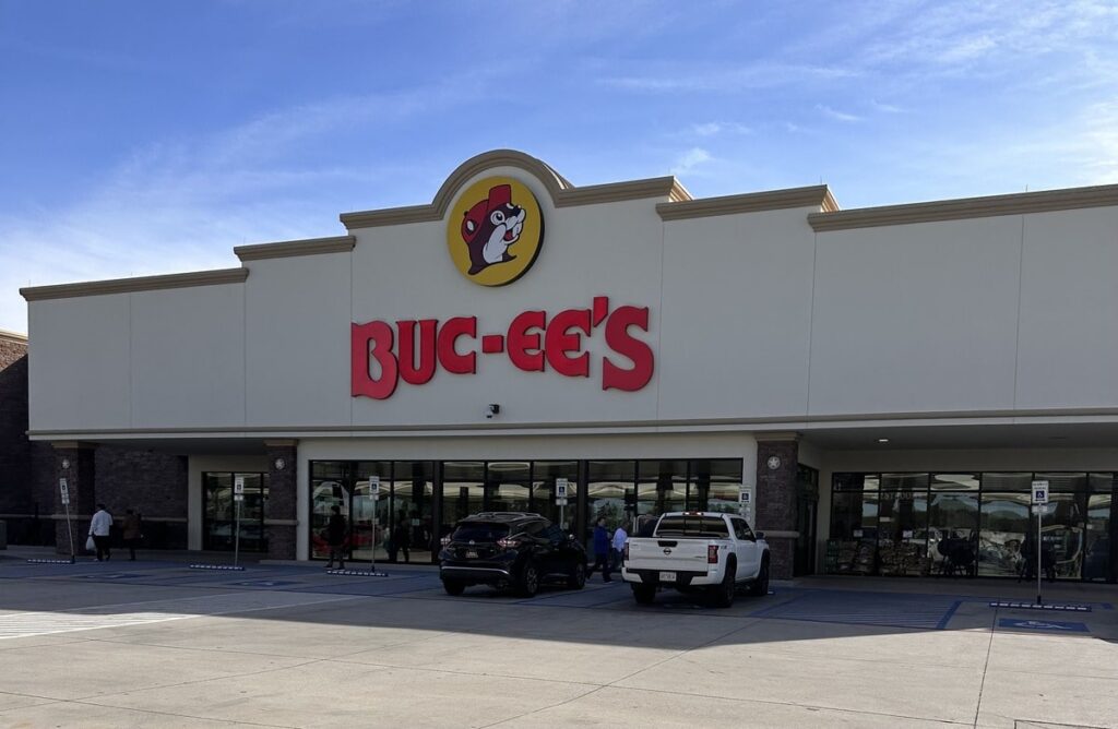 Buc-ees front entrance with cars parked out front and people walking out.
